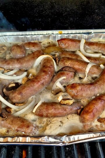 Beer Brats with onions in a pan on the grill