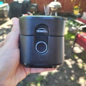 Thermacell Mosquito repeller being held in front of patio furniture and bbq