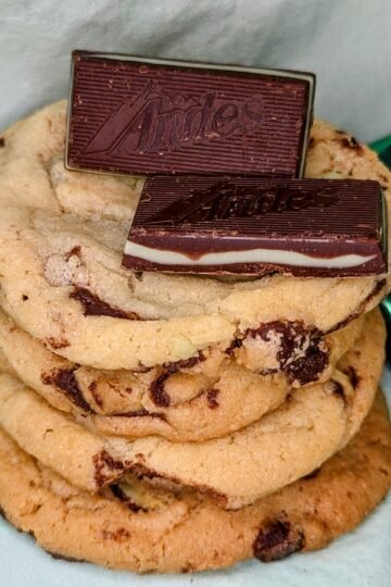 four stacked Andes mint chocolate chip cookies with two Andes mints on top and wrapped Andes mints in background