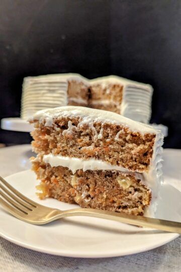 slice of carrot cake on a plate with gold fork, the rest of the cake is in the background