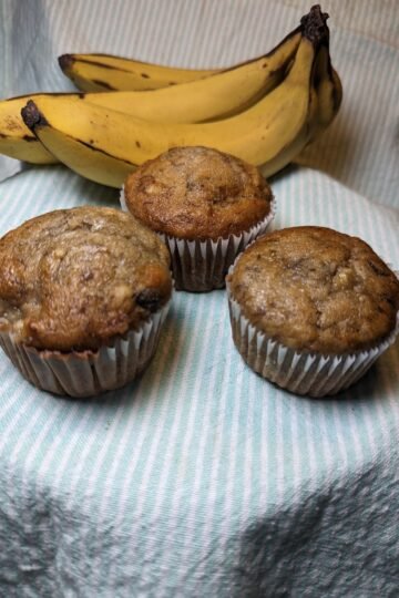 Three banana muffins with over ripe bananas in the background