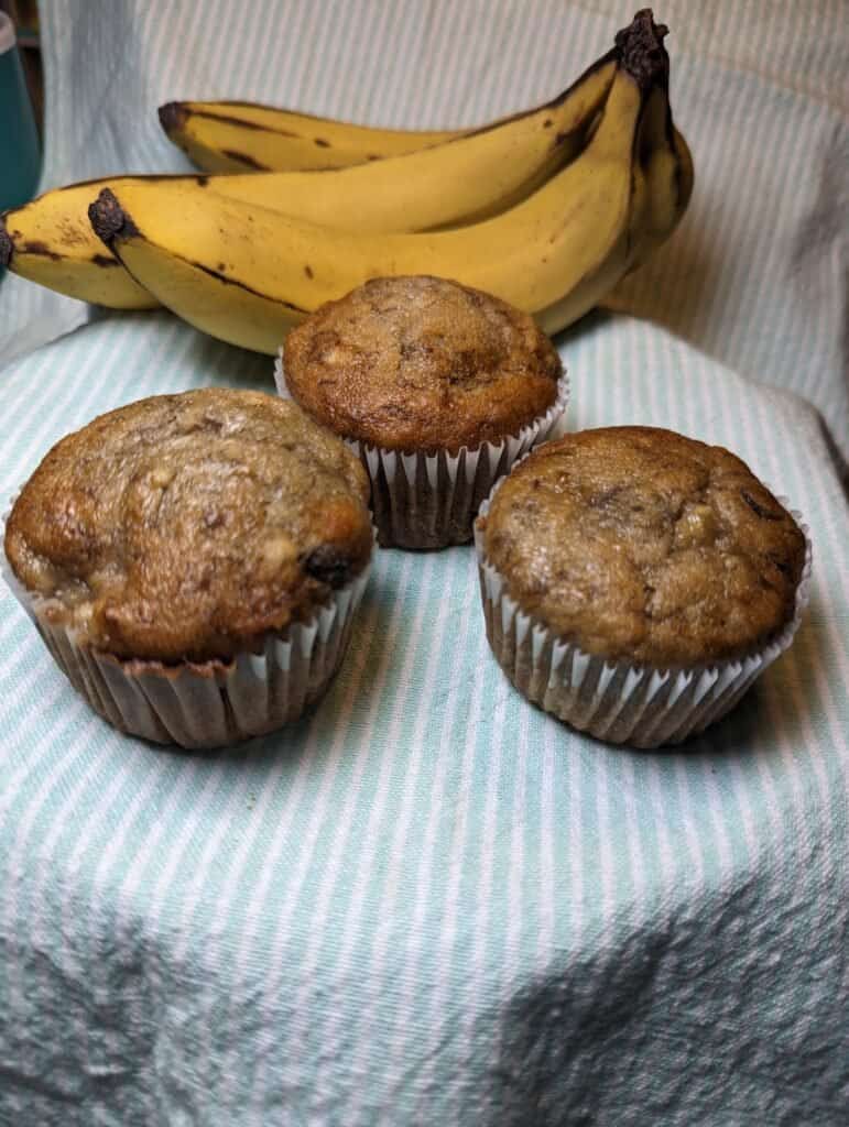 Three banana muffins with over ripe bananas in the background