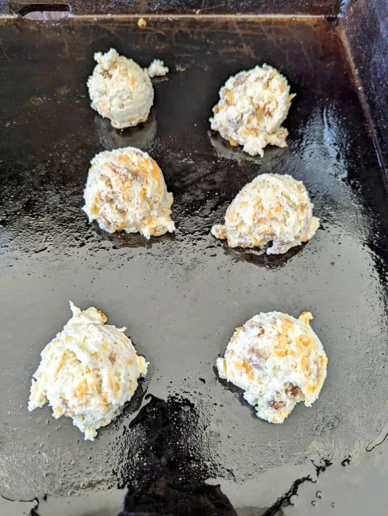six scoops of sausage cheddar biscuit dough on a flattop griddle