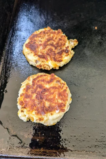 two sausage cheddar biscuits cooking on a flat top griddle