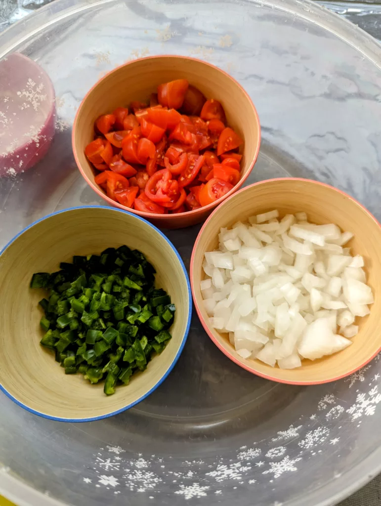 Three bamboo bowls each filled with one of the following: diced tomatoes in top bowl, diced jalapenos in the left bowl and diced white onion in the right bowl