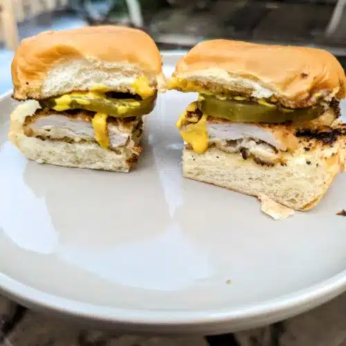 two pork schnitzel sliders with mustard and pickles on a white plate
