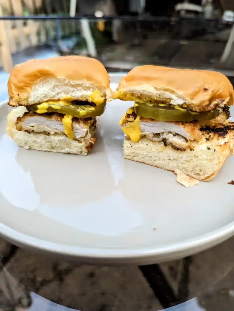 two pork schnitzel sliders with mustard and pickles on a white plate