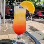 Malibu sunrise cocktail in a hurricane glass with an orange wedge on the rim.