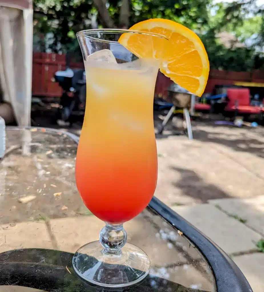 Malibu sunrise cocktail in a hurricane glass with an orange wedge on the rim.