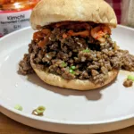Korean Beef Sloppy Joe on a plate with a jar of Kimchi in the background