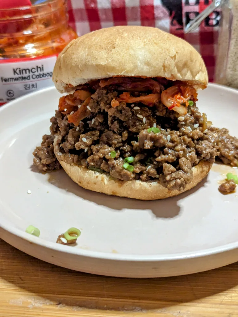 Korean Beef Sloppy Joe on a plate with a jar of Kimchi in the background