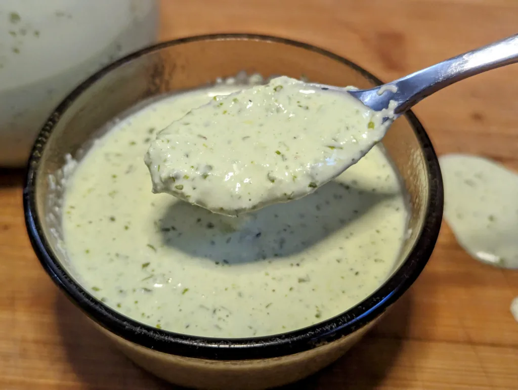 A small bowl of creamy cilantro jalapeno sauce with a spoon of sauce hovering above the bowl