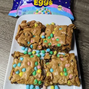 Plate of four Mini Egg Cookie Bars with a bag of mini eggs in the background.