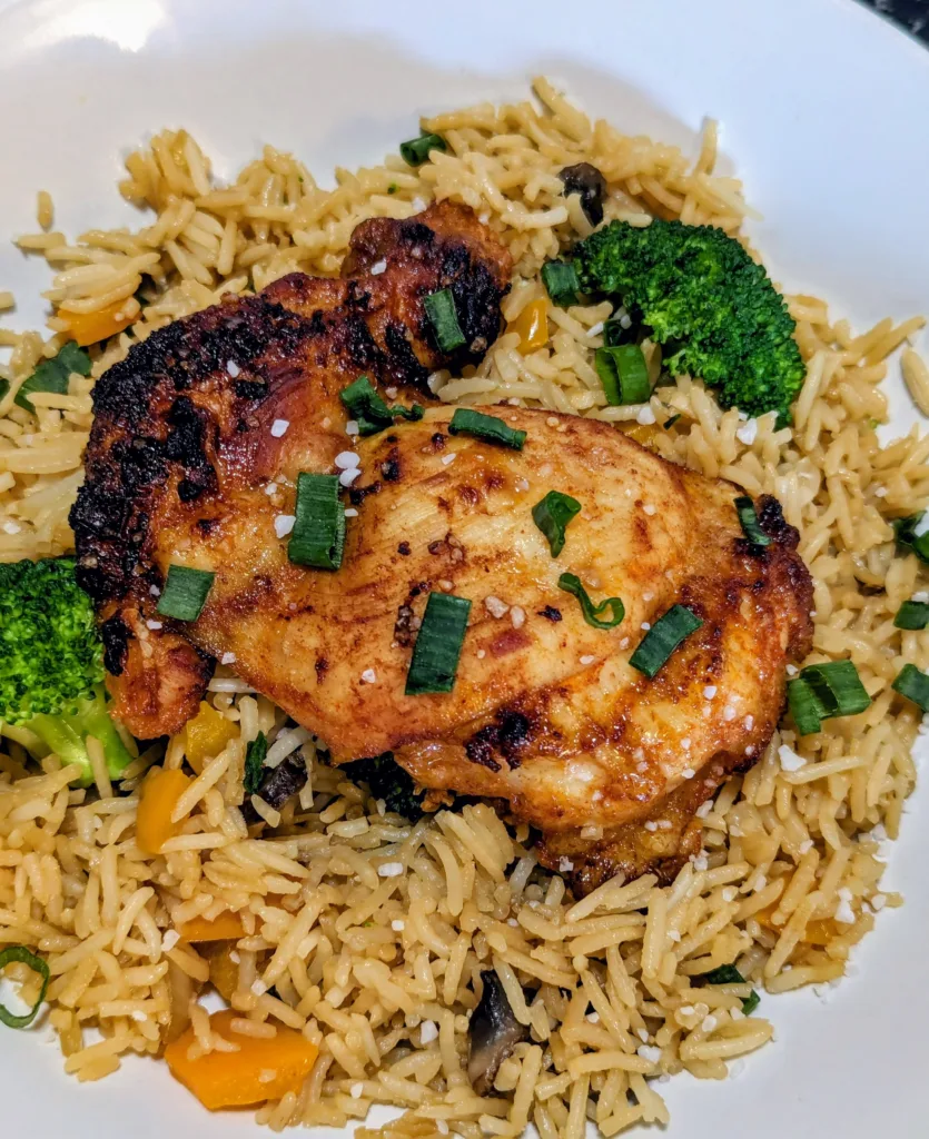 Gochujang chicken thigh on top of rice and broccoli, with green onion pieces sprinkled over top.