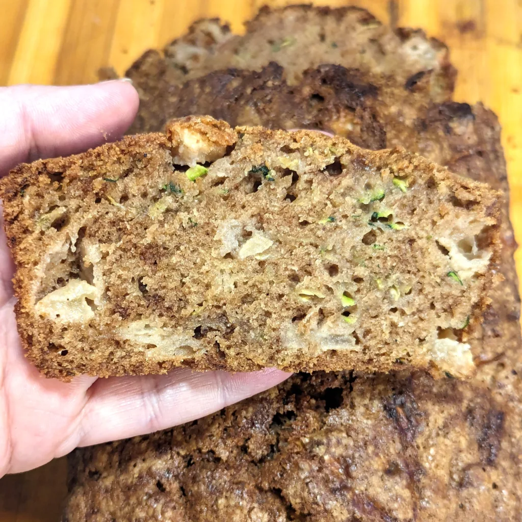 A slice of easy apple zucchini bread being held over the rest of the loaf