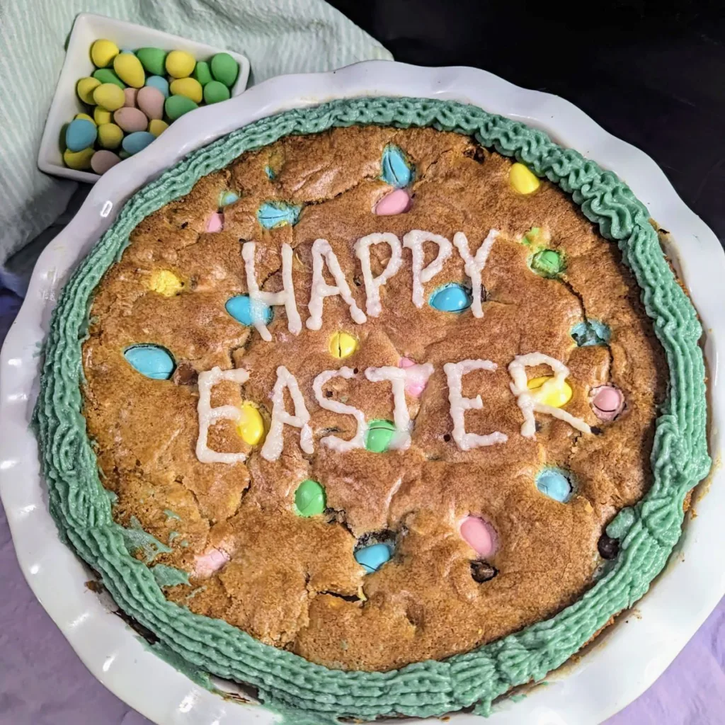 Giant Mini Egg Cookie with Happy Easter written in white icing across it. There is a bowl is Mini Eggs in the top left corner.