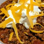 bowl of no bean chili with sour cream and shredded cheese on top.