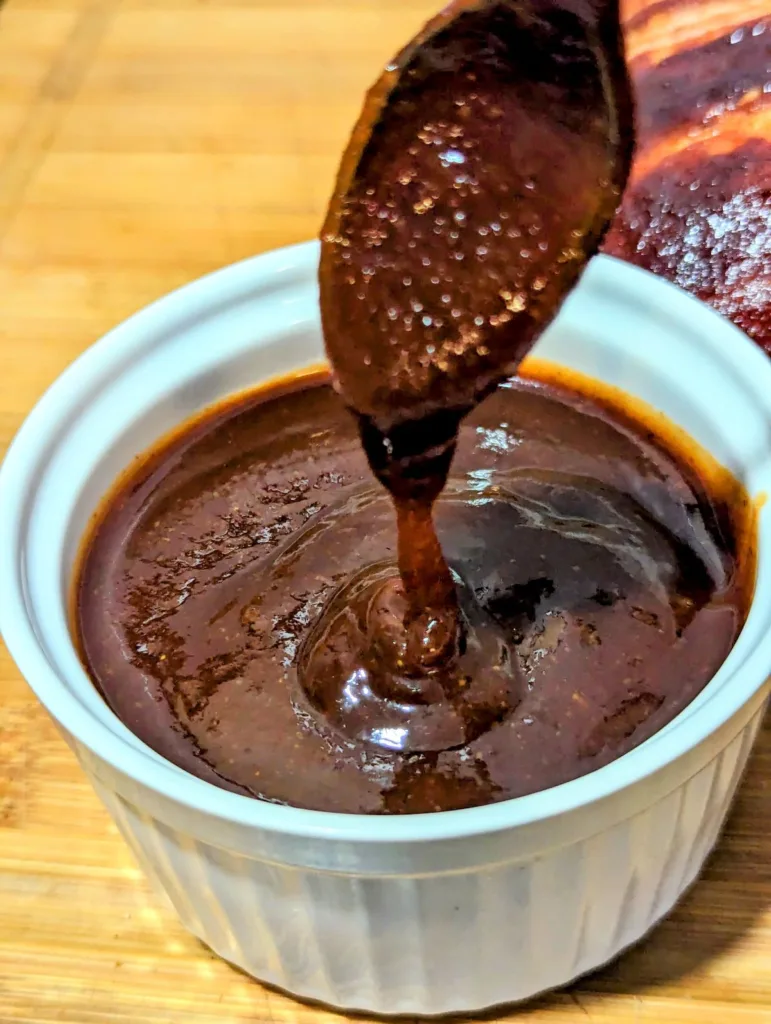 White ramekin filled with Apple Brown Sugar BBQ Sauce with a spoon of sauce pouring into the bowl.