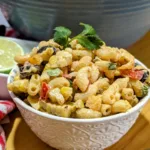 Bowl of Tex-Mex Macaroni Salad with cilantro leave on top and a sliced lime in the background