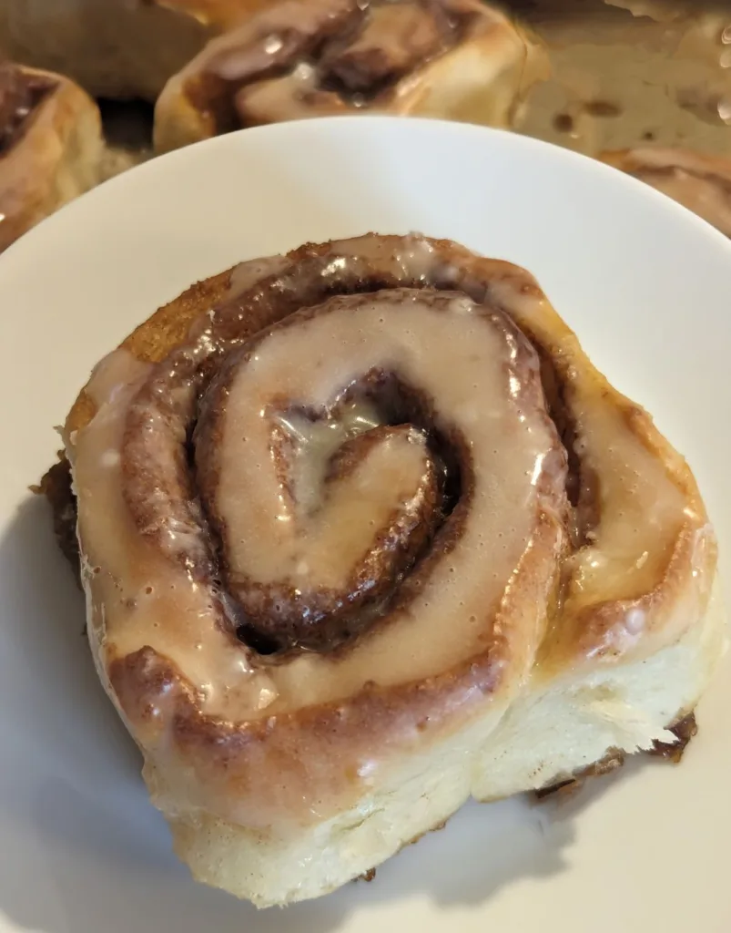 Easy Homemade Cinnamon Bun on a plate with a blurred vision of the pan of cinnamon buns in the background