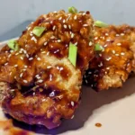 Fried chicken with sweet and spicy gochujang sauce over it, along with sesame seeds and chopped green onions.