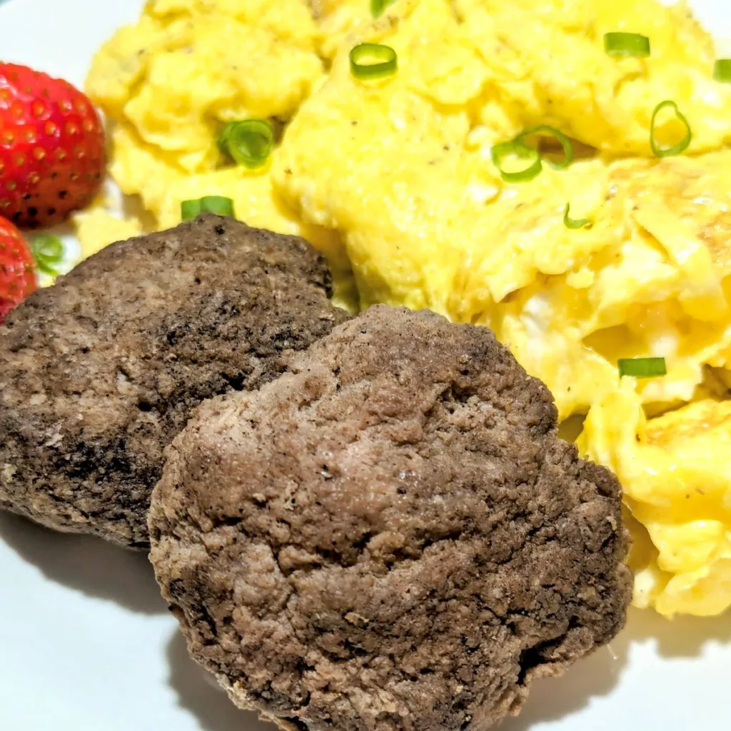 two griddle turkey breakfast patties on a plate with scrambled eggs and strawberries.