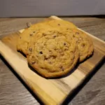 four skor chocolate chip cookies on a square wooden cutting board