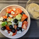 bowl of Greek salad with a small bowl of Greek Salad Dressing.